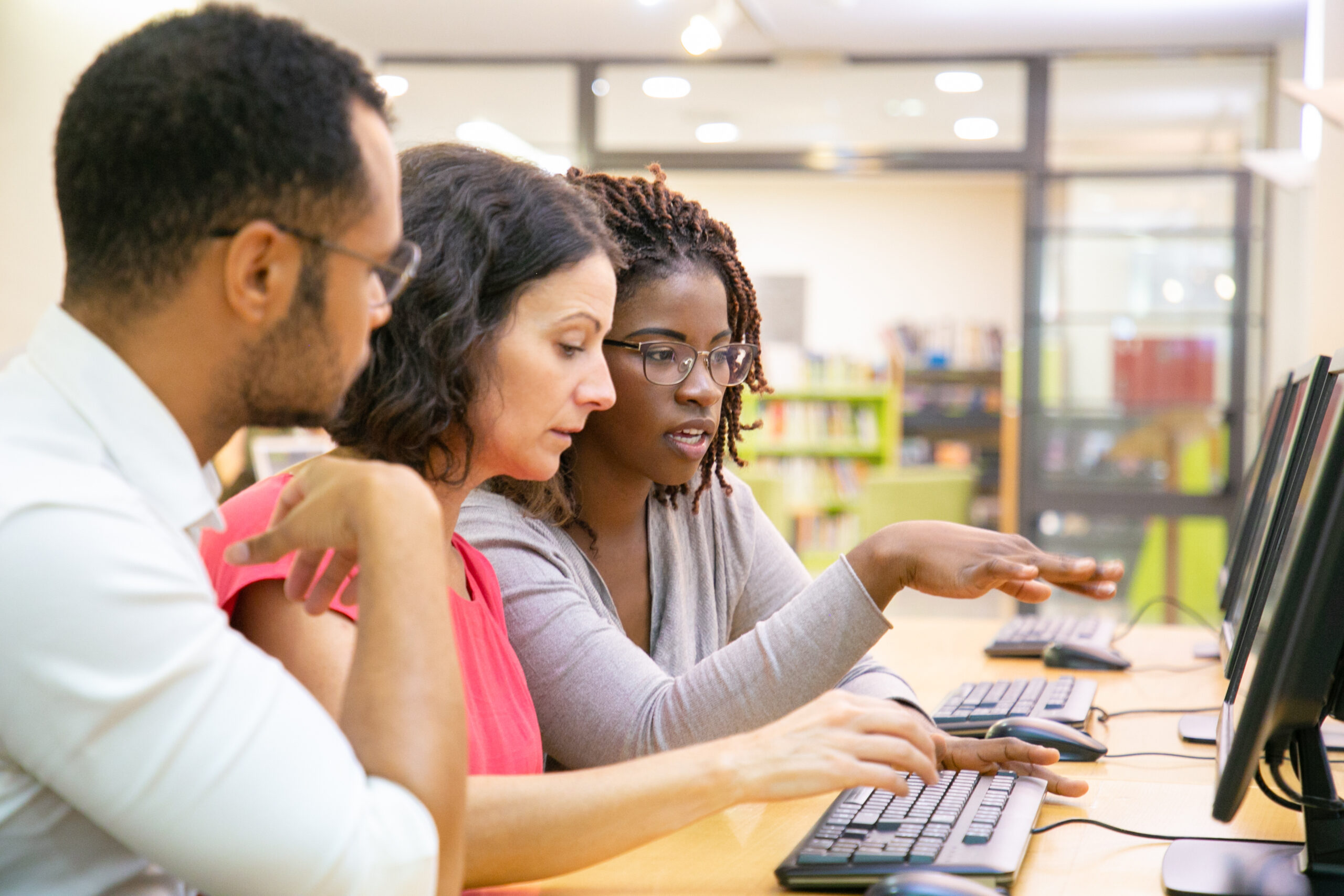 Instructor explaining corporate software specific to trainees in computer class. Man and women sitting at table, using desktop, pointing at monitor and talking. Training concept