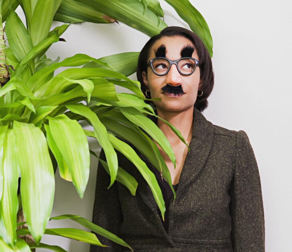 Businesswoman hiding behind plant wearing disguise