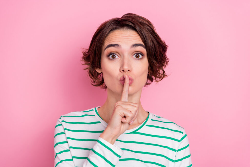 Portrait of attractive mysterious girl showing shh sign keep silence isolated over pink pastel color background