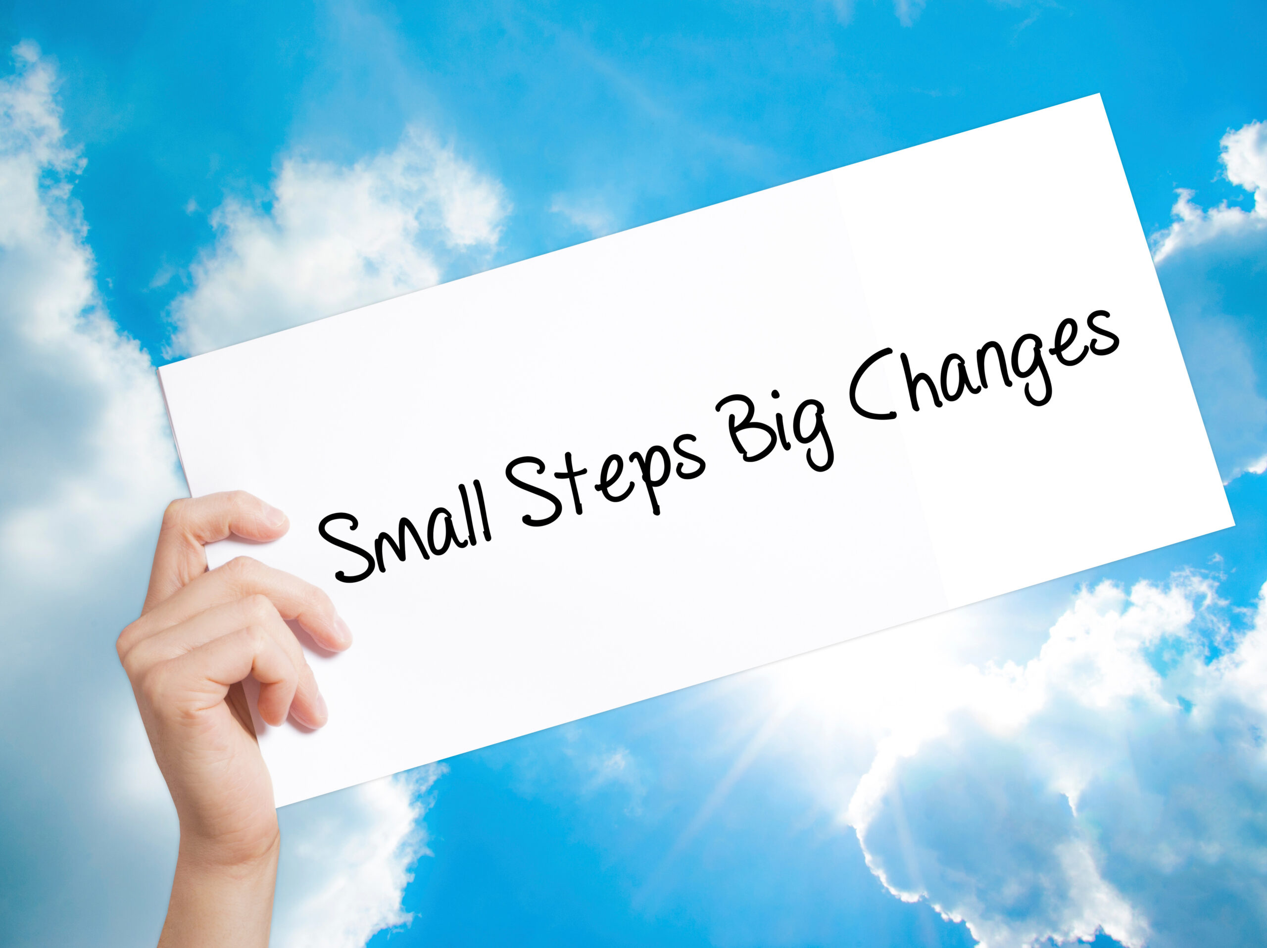 Small Steps Big Changes Sign on white paper. Man Hand Holding Paper with text. Isolated on sky background