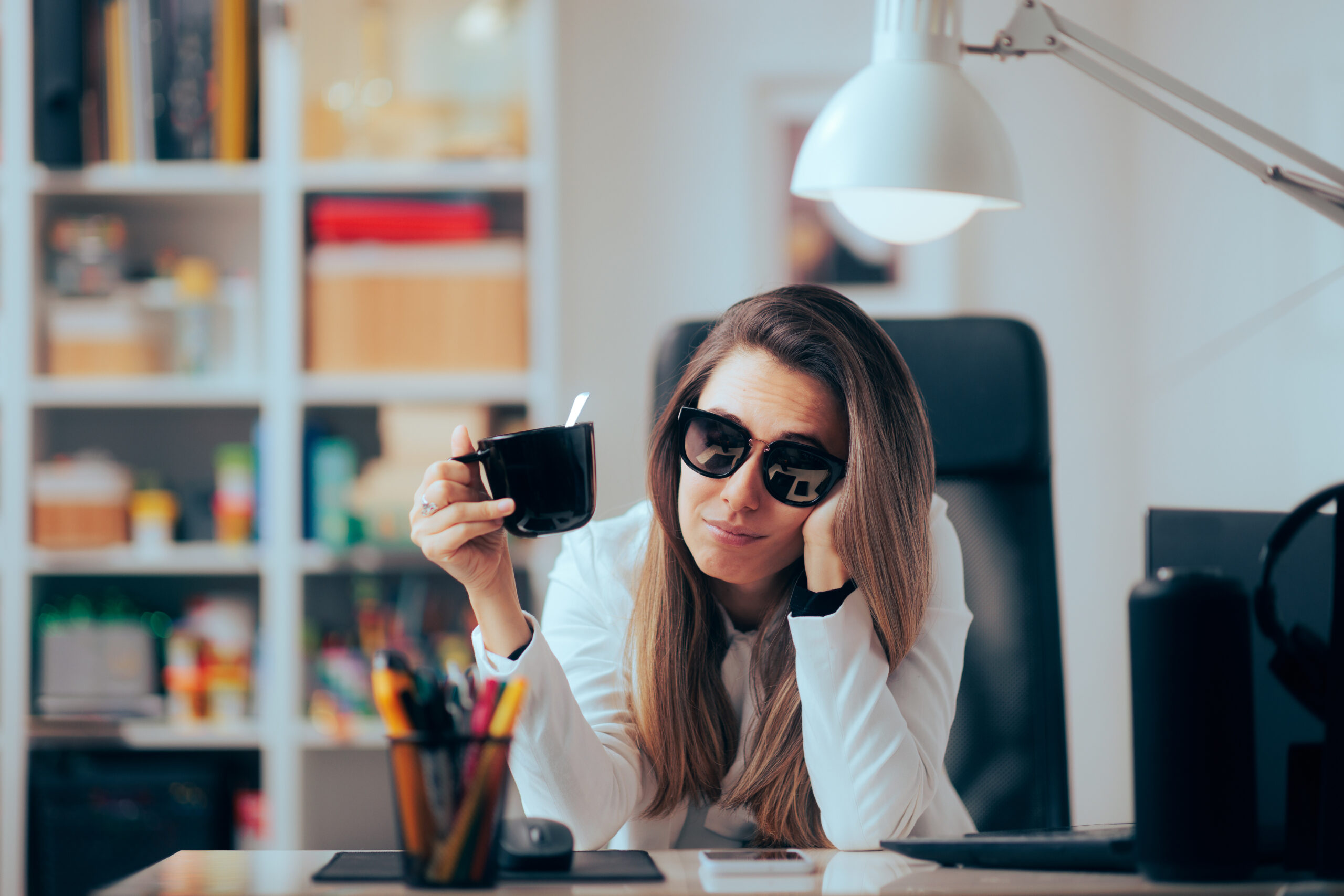 Hangover Woman Drinking Coffee Wearing Sunglasses in the Office. Sleepy businesswoman working after a night of partying