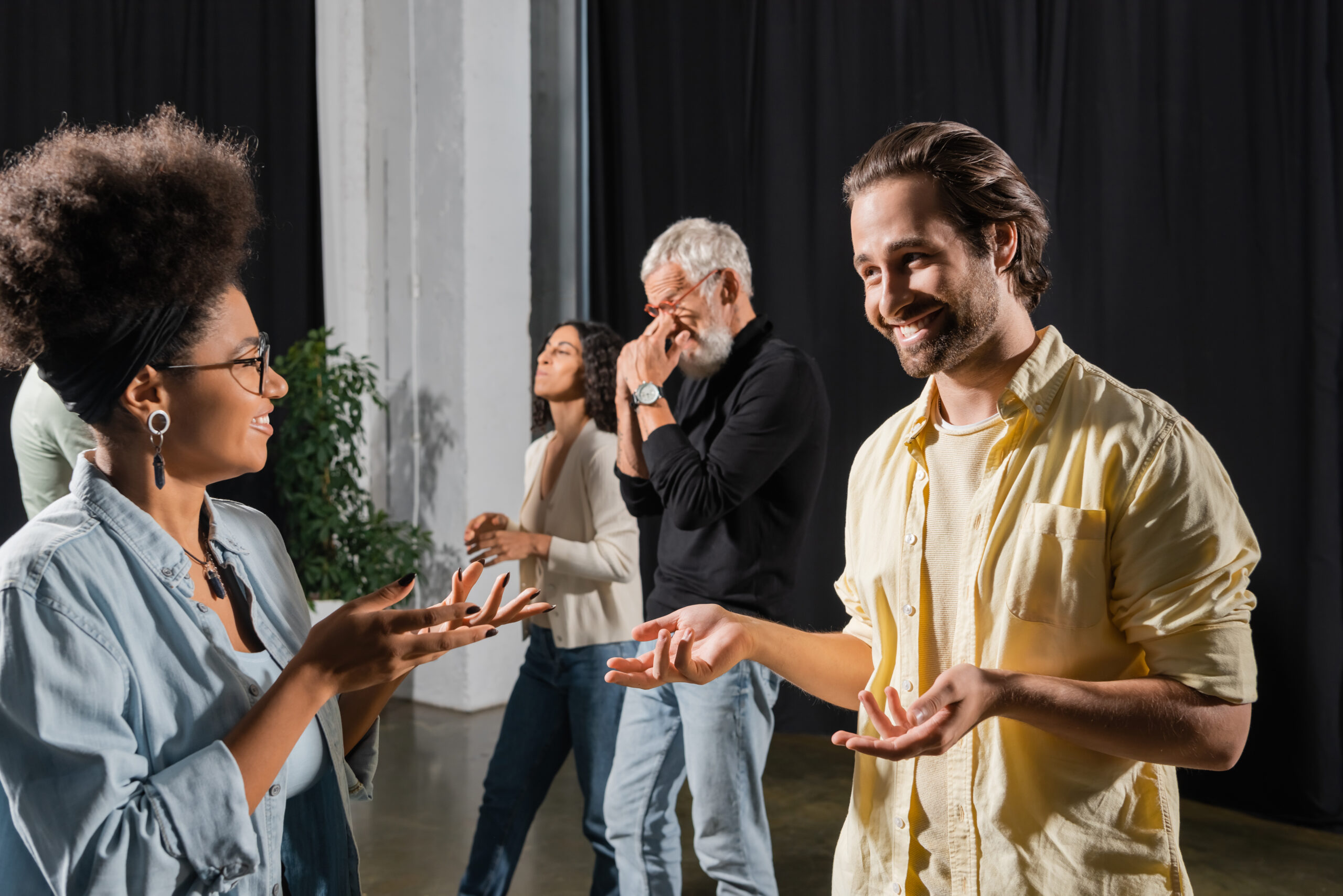 smiling brunette man talking to african american woman near interracial colleagues in acting school.