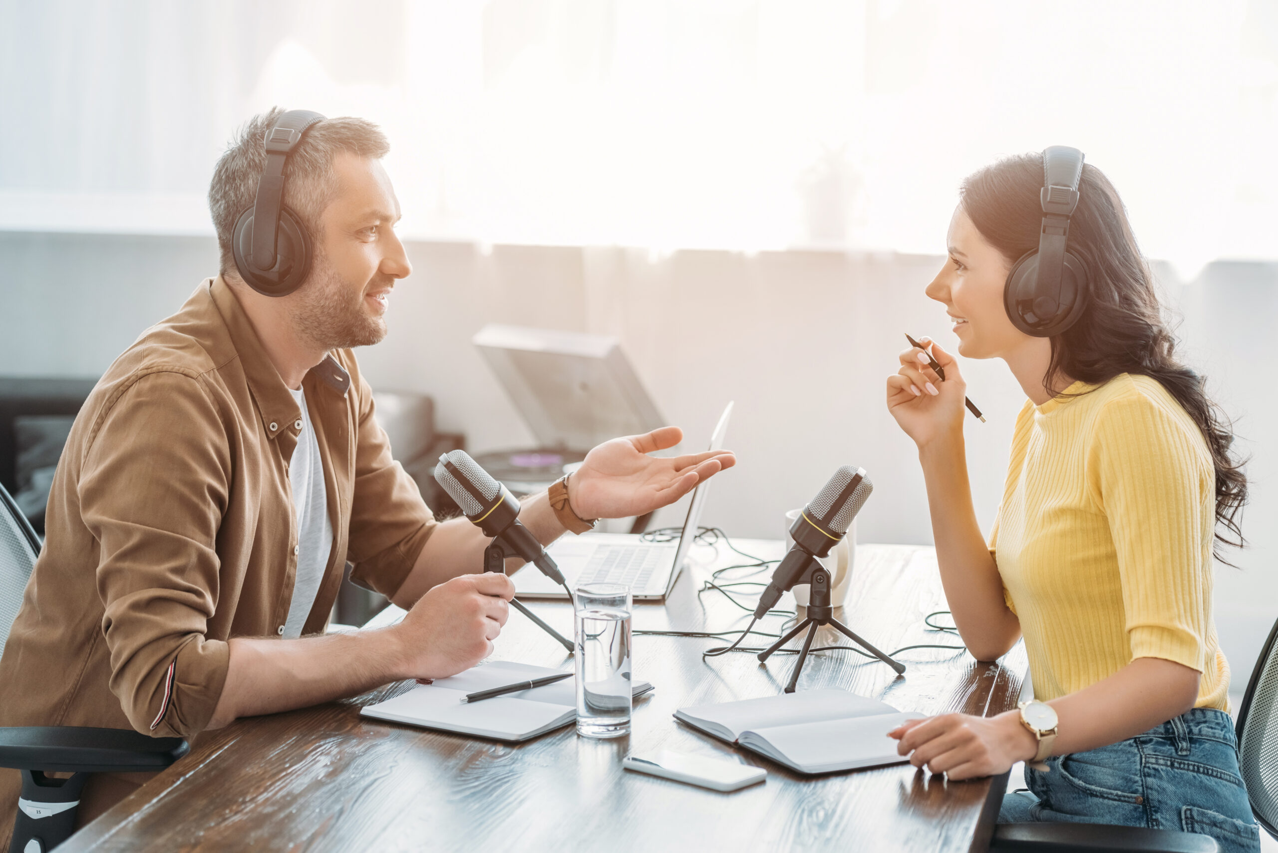 two radio hosts in headphones talking while recording podcast in radio studio