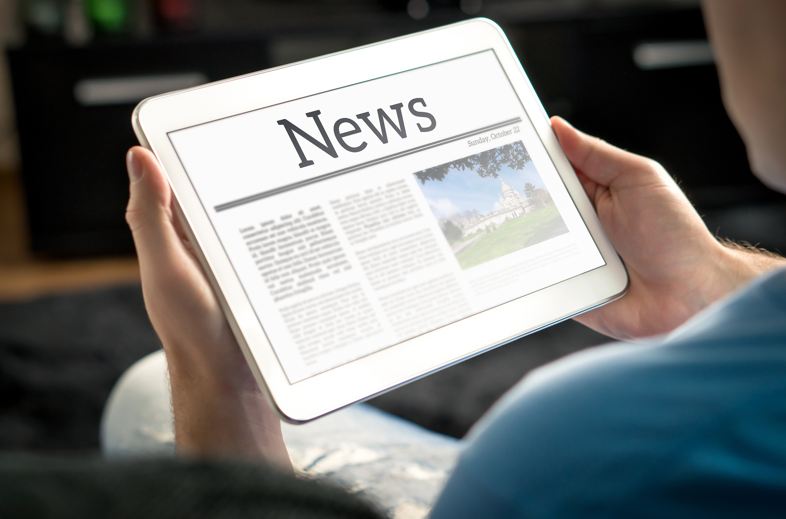 Man reading the news on tablet at home. Imaginary online and mobile news website, application or portal on modern touch screen display. Holding smart device in hand.