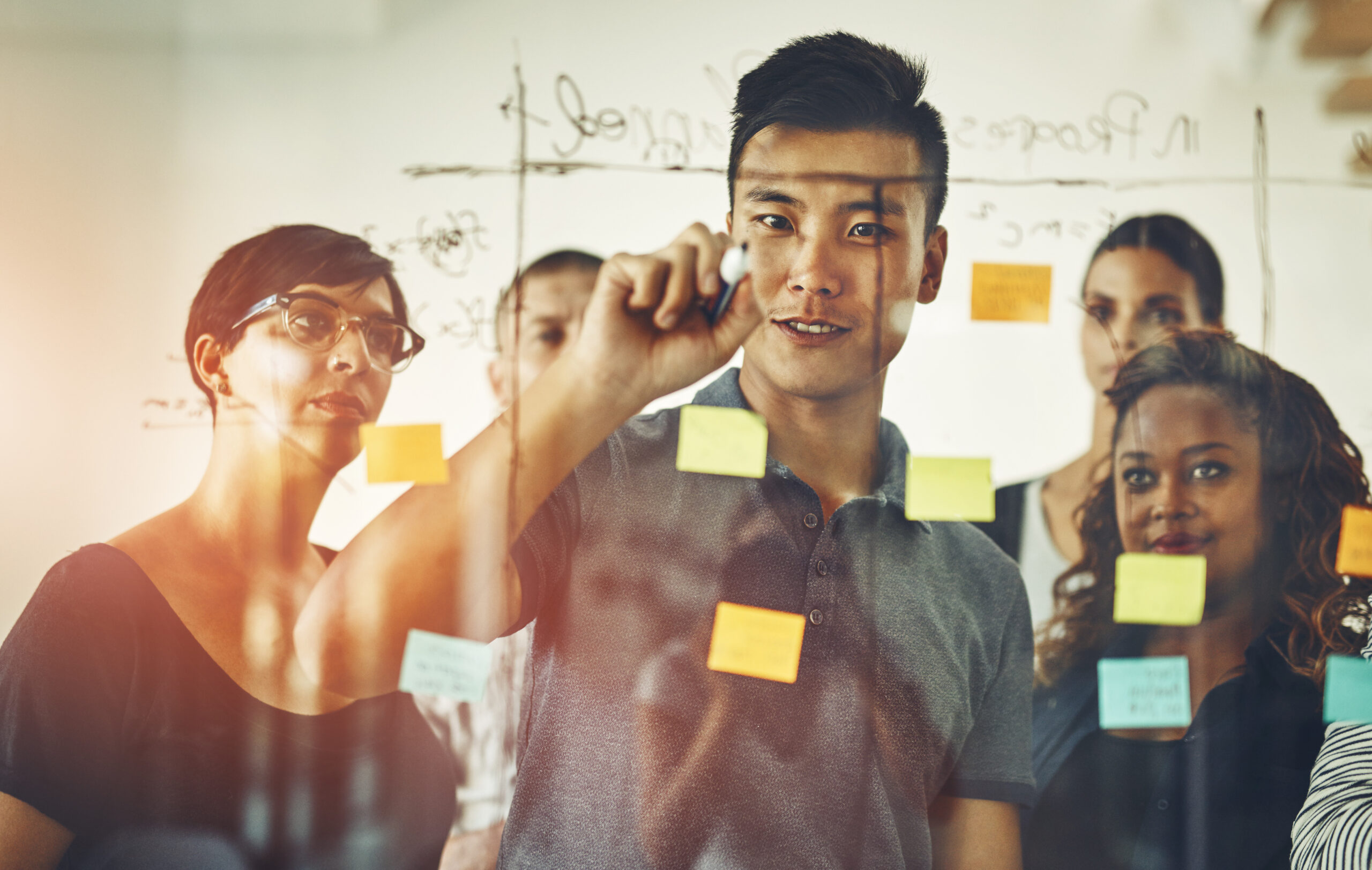 Team leader planning and writing on sticky notes while brainstorming, talking and sharing vision or ideas. Diverse group of creative business people meeting together to market new startup company